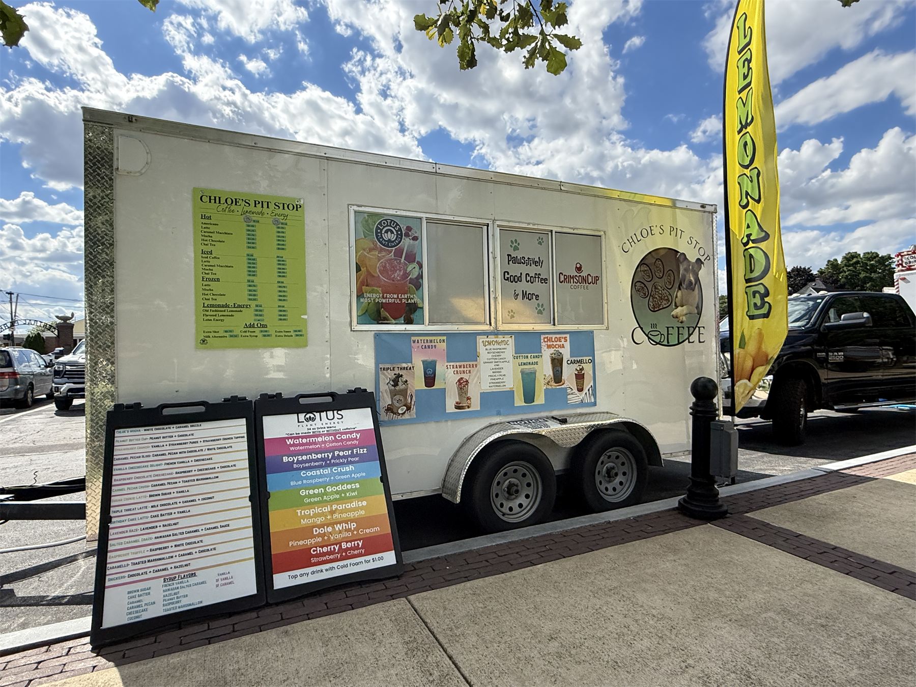 The Chloe's Pit Stop coffee trailer set up at an event, with printed menu boards, Crimson Cup signage in the window, and a tall yellow lemonade flag